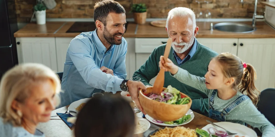 Uśmiechnięta rodzina siedzi przy stole podczas wspólnego posiłku, wyglądając na zdrową i pełną energii — scena ilustruje efekt dbania o jelita dzięki produktowi Bactoflor Omni.